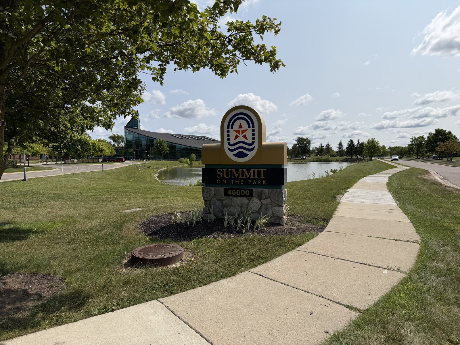 Entrance sign for Summit on the Park in Canton, Michigan, with the recreation building and pond in the background.