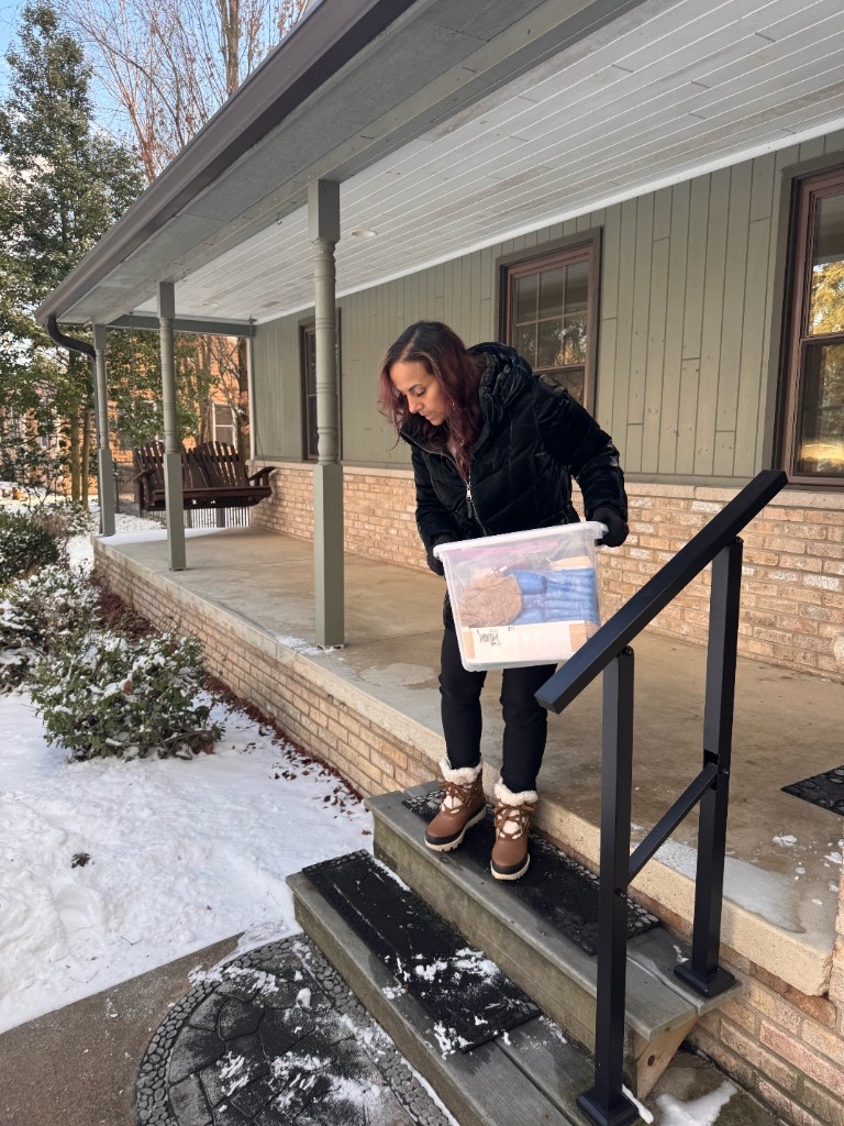 Derica Wade carrying a storage bin down snowy porch steps while helping a client during a move in Southeast Michigan