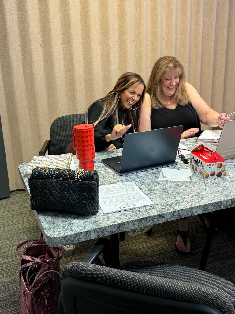 Derica Wade and Shelley Ball laughing together while reviewing documents at a Hearts to Homes team meeting