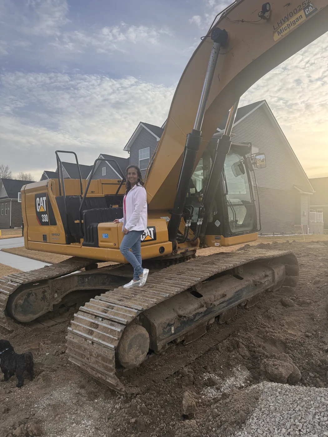 Excavator working on a residential homesite with soil piles and survey stakes marking the new construction footprint