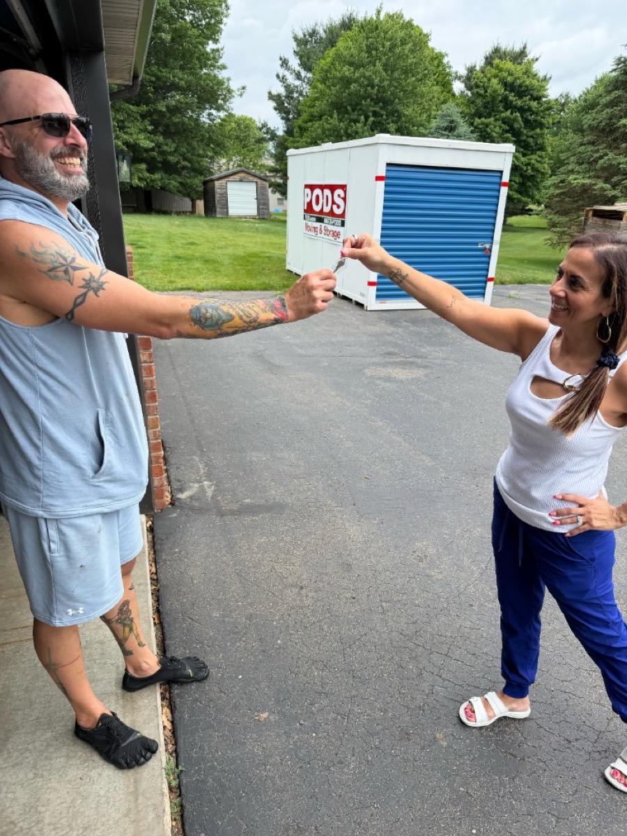 Hearts to Homes Associate Broker handing house keys to Michigan home buyers on closing day with a moving pod in the driveway