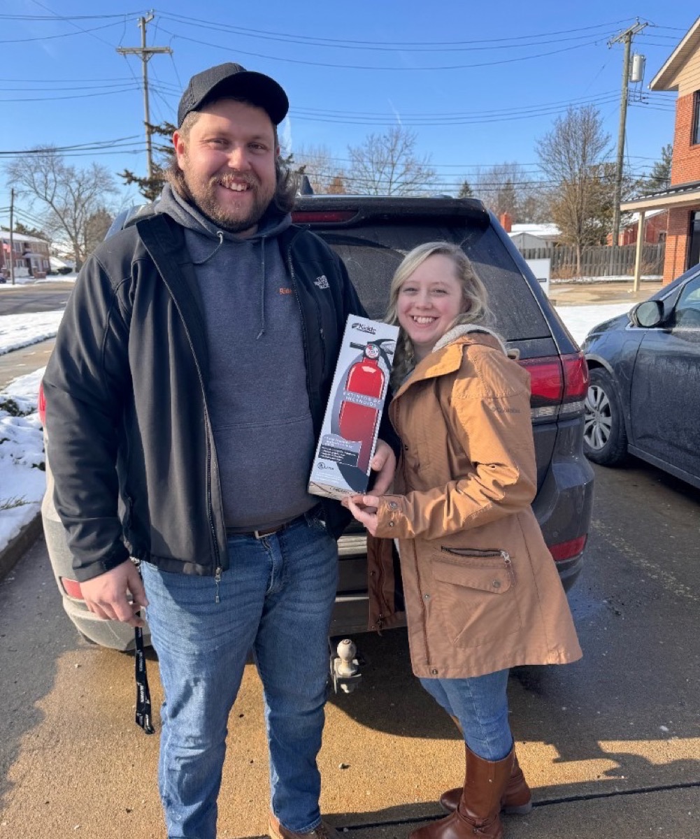 New Michigan homeowners receiving a fire extinguisher as a practical housewarming gift after closing on their home