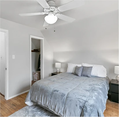 Primary bedroom after staging: neatly styled bed with grey quilt and white pillows, matching nightstands with lamps, hardwood floors, and a calm, clutter-free presentation
