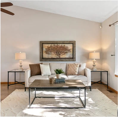 Traditional living room after staging: cream sofa with coordinated pillows, tree wall art, wood-and-metal coffee table, matching end tables, and an open, buyer-ready layout