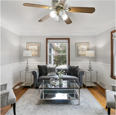 Living room after staging: grey tufted sofa with coordinated pillows, glass end tables with lamps, area rug, and a clear seating layout in the same teal-and-white room